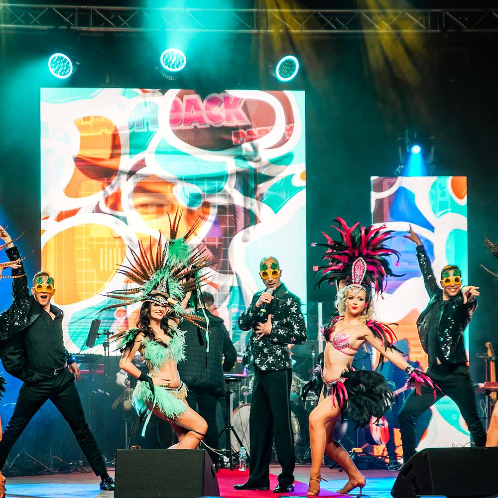Latin Carnival – tancerki w karnawałowych pióropuszach z wokalistą na scenie, Shine Show Art Agency